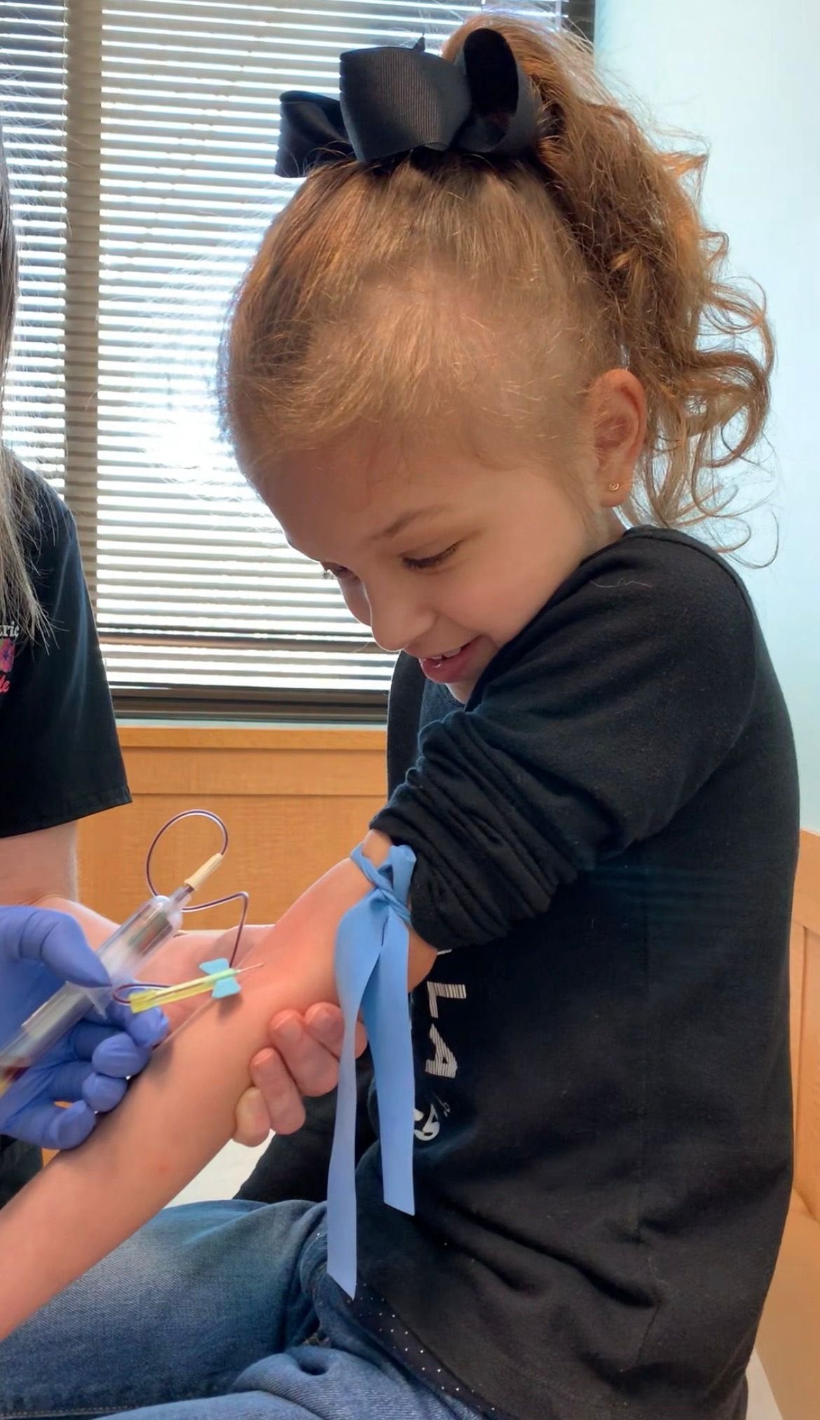 Anabella as a young girl, smiling during a blood draw at the hospital