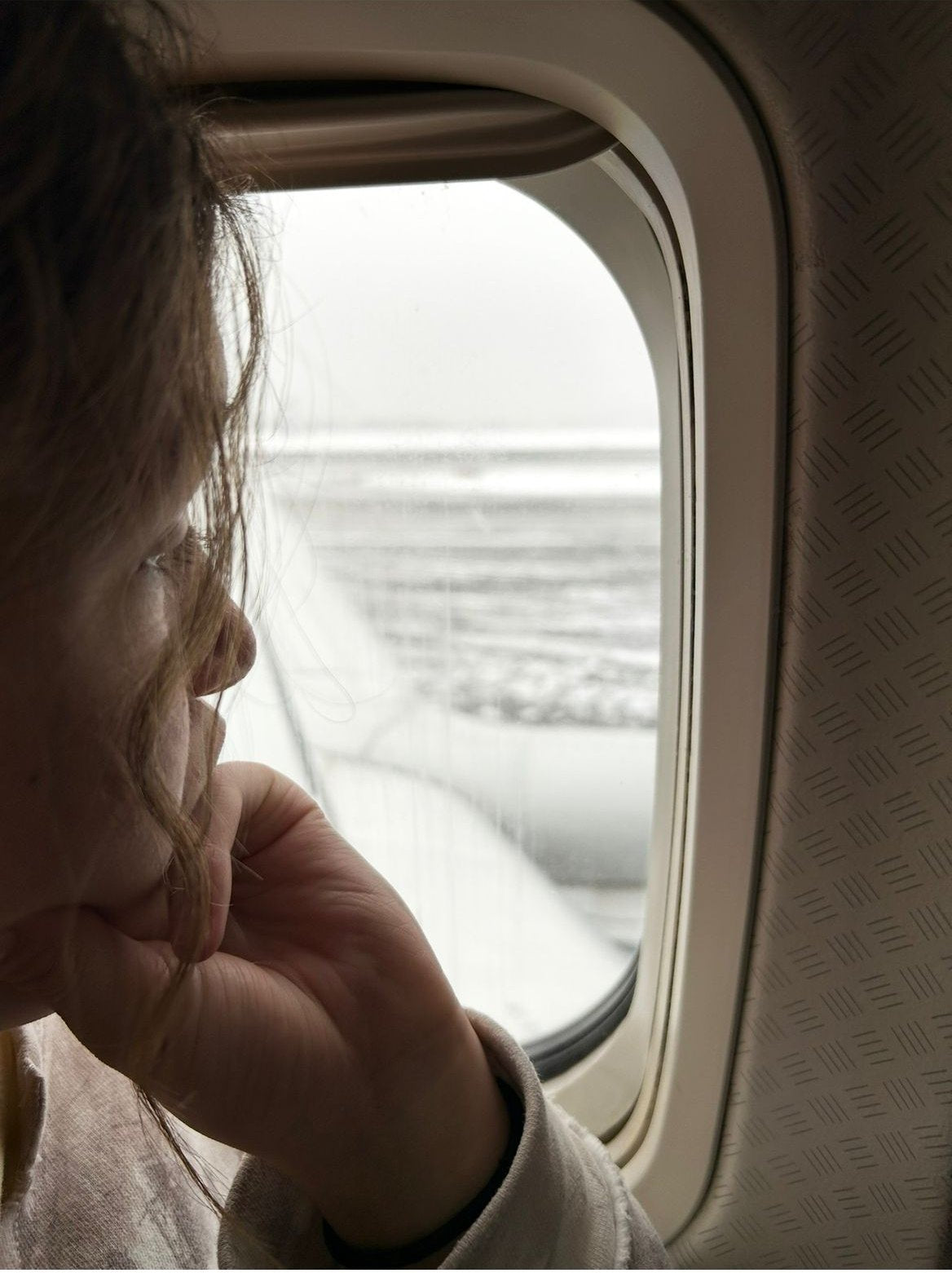 Anabella looking out of an airplane window at a snow-covered runway